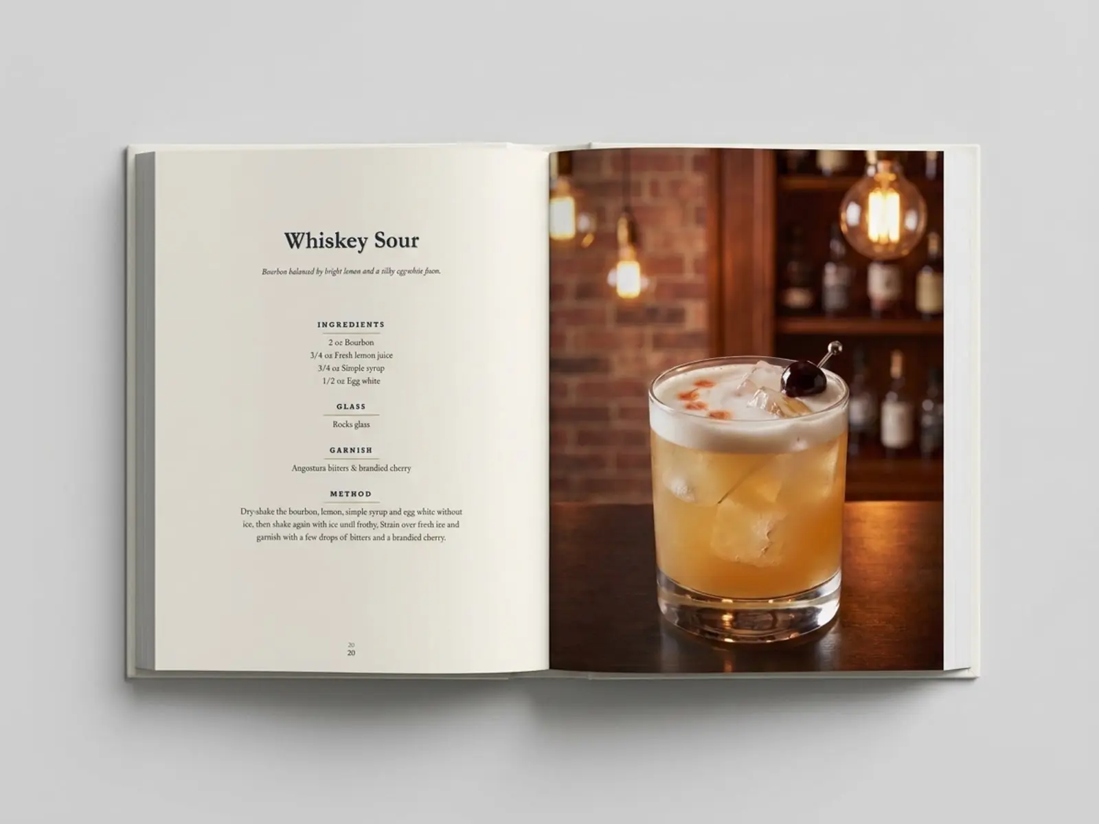 A real printed copy of Classic Cocktails lying open at the Whiskey Sour recipe and its photograph