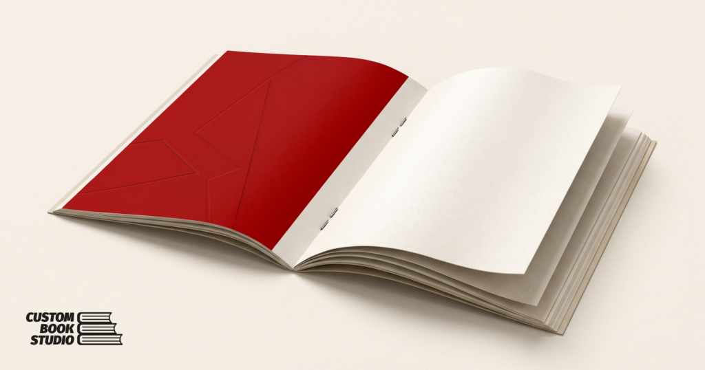 Custom Book Studio — an open saddle-stitched booklet held by two metal staples in the centre fold (watermarked).
