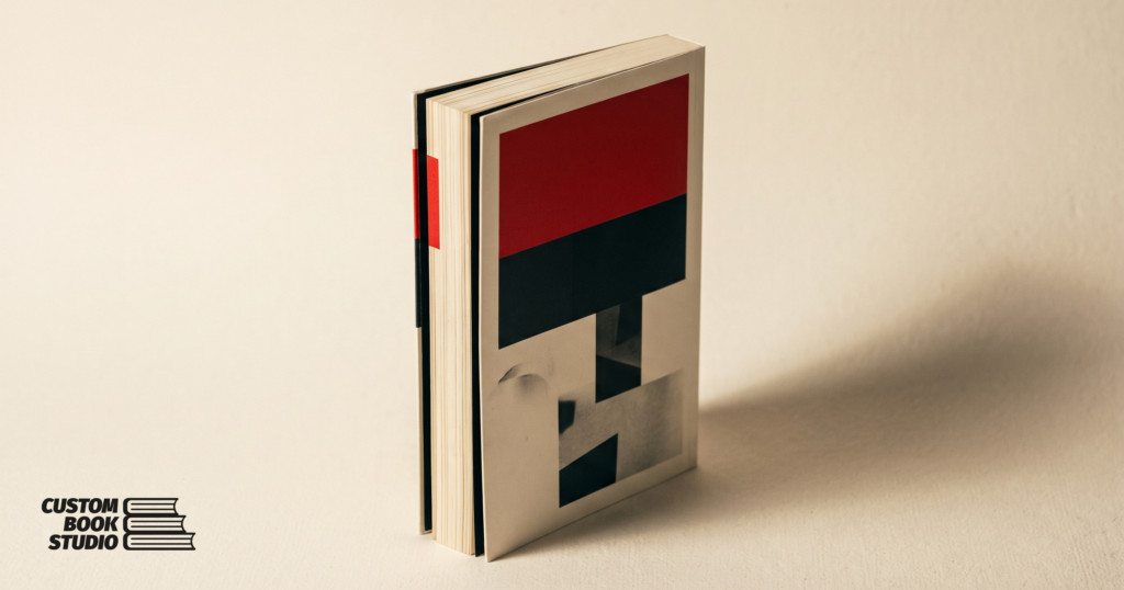 Custom Book Studio — a softcover perfect-bound paperback with a red cover and a flat glued spine (watermarked).