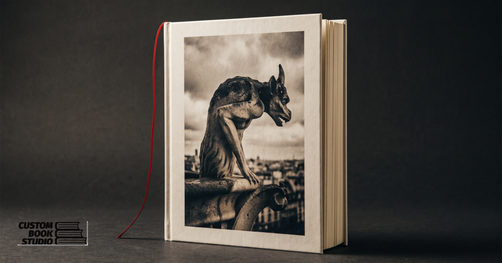A hardcover photography book, Watchers in Stone, standing on a dark studio surface with a concrete gargoyle on its cover